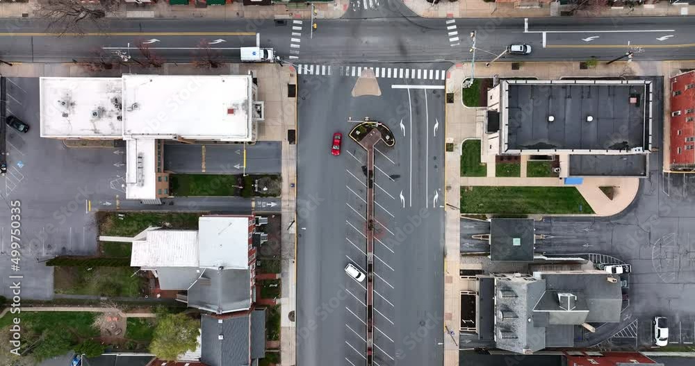 Aerial tracking of red car driving through American city, past USA flag in town square. Aerial tracking of red car driving through American city, past USA flag in town square.