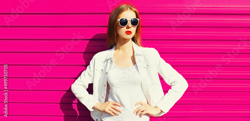 Portrait of beautiful young woman with red lipstick wearing white shirt, sunglasses on pink background, blank copy space for advertising text