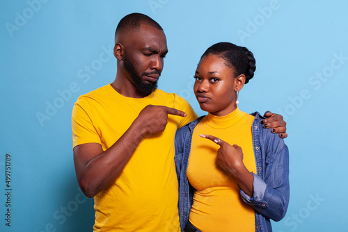 African american people pointing index fingers at each other in studio. Playful couple showing sideways directions and sharing embrace in front of camera. Romantic partners in relationship photo