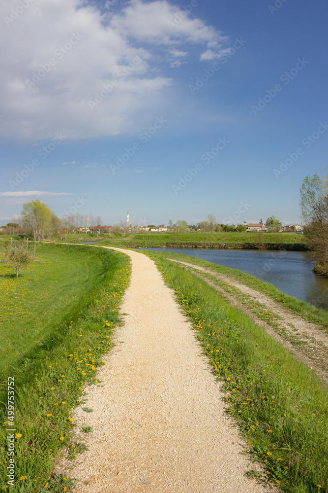 Beautiful bike path along the river. White gravel path with grassy edges. Cordignano, Italy. Vertical image.