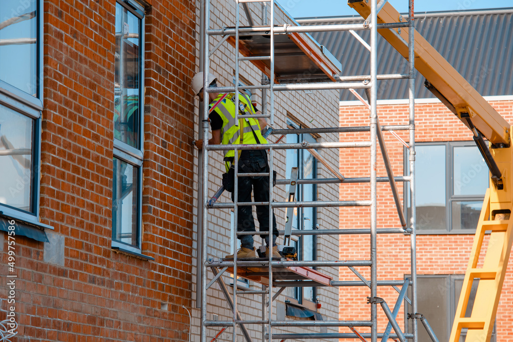 Construction workers using aluminium mobile scaffold tower and safety harness to work at height. Working at height safety regulation Construction workers using aluminium mobile scaffold tower and safety harness to work at height. Working at height safety regulation
