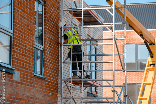 Fotografie Construction workers using aluminium mobile scaffold tower and safety harness to work at height