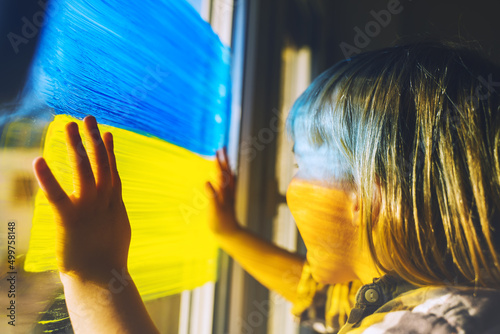 Fototapeta Little child with hands on yellow-blue flag image of Ukraine on window