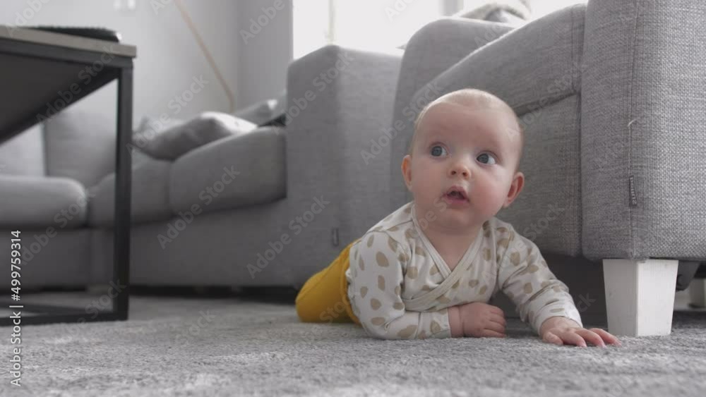 Caucasian toddler turns on to front on living room carpet Caucasian toddler turns on to front on living room carpet