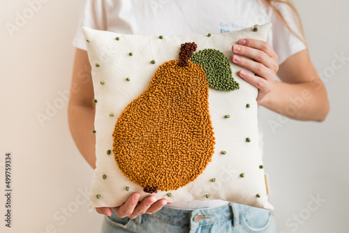 Close-up of woman hands holding pillow. Punch needle embroidery pillow diy. Product is made according to the technique pushing woolen threads on foundation fabric with needle with wood handle