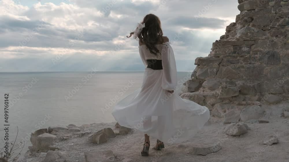 A young girl with dark hair, dressed in a white dress, is spinning on the top of the mountain, the wind blowing her hair and dress, and smiling - harmony, adventure, freedom, 4k video. slow motion A young girl with dark hair, dressed in a white dress, is spinning on the top of the mountain, the wind blowing her hair and dress, and smiling - harmony, adventure, freedom, 4k video. slow motion