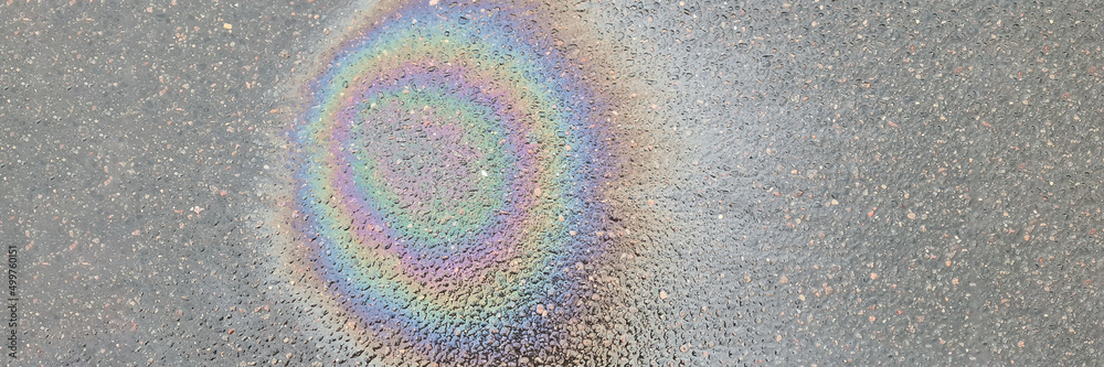 Rainbow stain on wet asphalt from machine oil closeup background