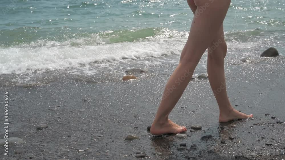 Tanned slender female legs. A young woman walks along the seashore. The concept of summer holidays. Tanned slender female legs. A young woman walks along the seashore. The concept of summer holidays.