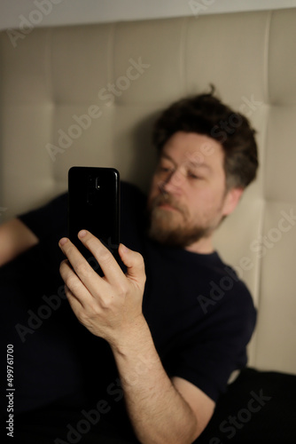 man's hand holding a cell phone while lying on a bed