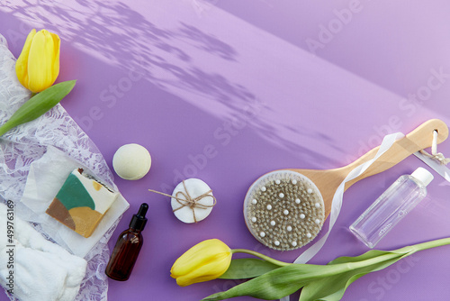 SPA beauty treatment complete hygiene accessories, natural soap, essence oil, massage brush, bath bomb, sponges on purple background with tulips. Copy space