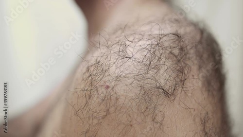 Young man with a naked body strokes the hair on his shoulder with his hand. A man has a lot of body hair.