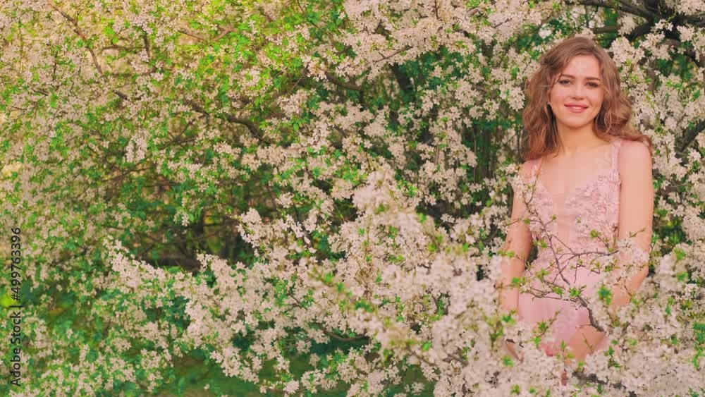 Portrait young beautiful red-haired cute woman looking at camera, smiling romantic face. Fashion model posing girl princess. Spring nature blooming tree, white flowers, summer green leaves. Pink dress