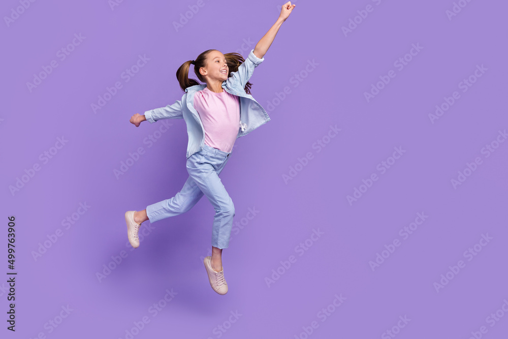 Fototapeta premium Photo of cute excited little school girl wear denim shirt jumping high holding arm empty space isolated purple color background