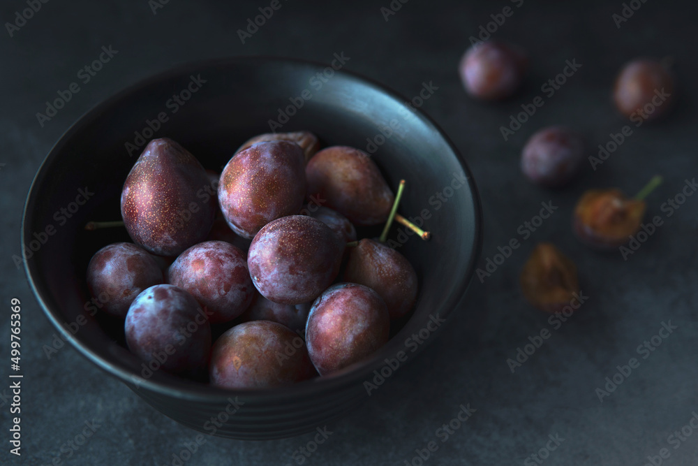 Fototapeta premium Closeup Heap of fresh picked plums in a black bowl with dark blue grey background.