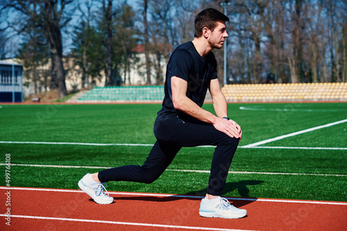 Man in sport clothers does a warm-up exercises at stadium track before jogging outdoors, Healthy lifestyle