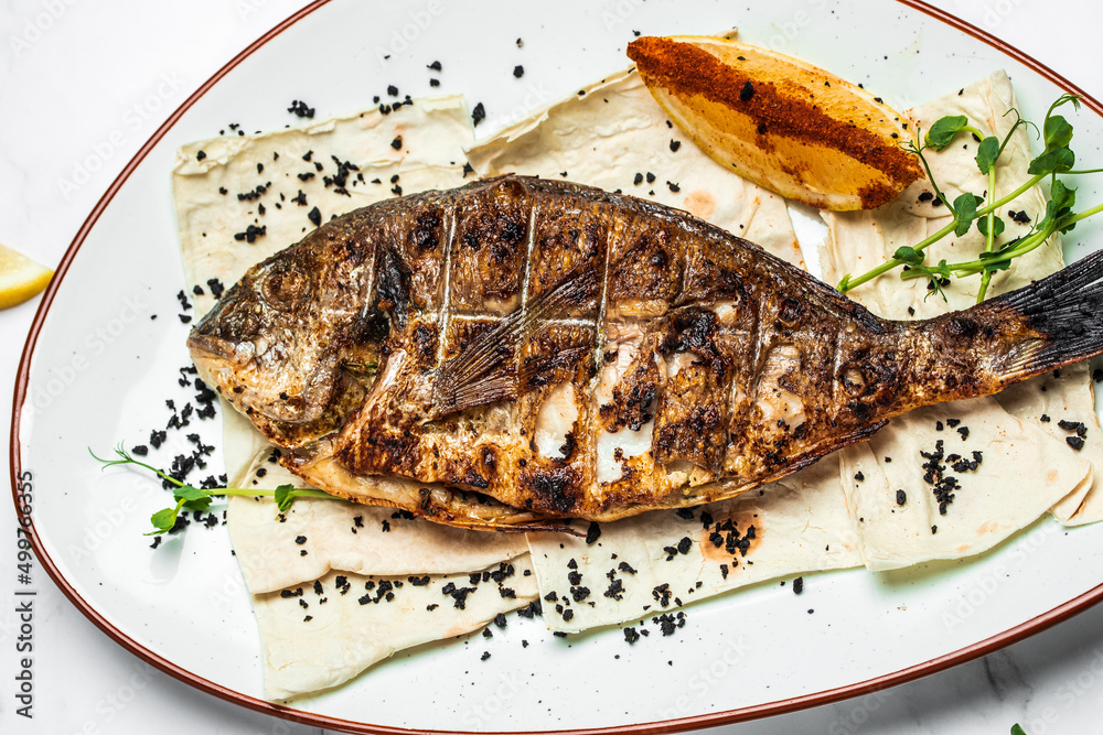 Plate with prepared dorado fish, Whole Bbq sea bream baked. Dorado grill. Ketogenic, keto or paleo diet lunch, Healthy food trend. Top view Plate with prepared dorado fish, Whole Bbq sea bream baked. Dorado grill. Ketogenic, keto or paleo diet lunch, Healthy food trend. Top view