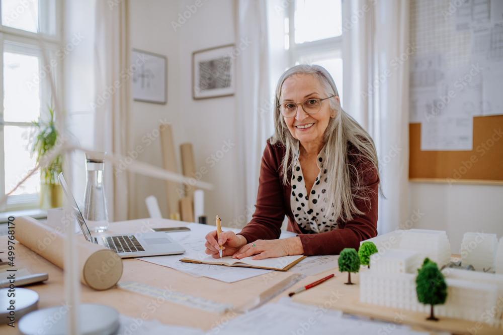 Senior woman architect with model of houses in office writing notes. Senior woman architect with model of houses in office writing notes.