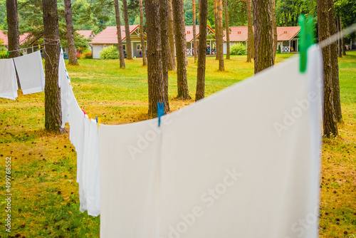 close up photo of fresh white laundry hanging on a washing rope with clothespin between pine trees outdoor in a summer camp in a forest, focus on background