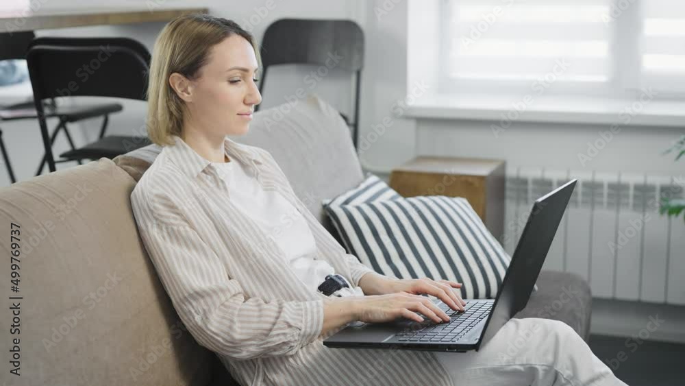 Pleasant young woman in her apartment using a modern laptop for work, online shopping, and entertainment Pleasant young woman in her apartment using a modern laptop for work, online shopping, and entertainment