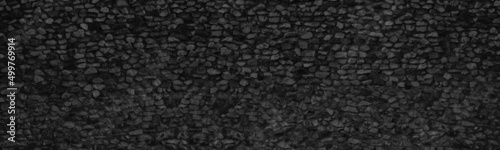 Old black stone wall wide panoramic texture. Rough crushed rock masonry gloomy backdrop. Dark gray abstract background