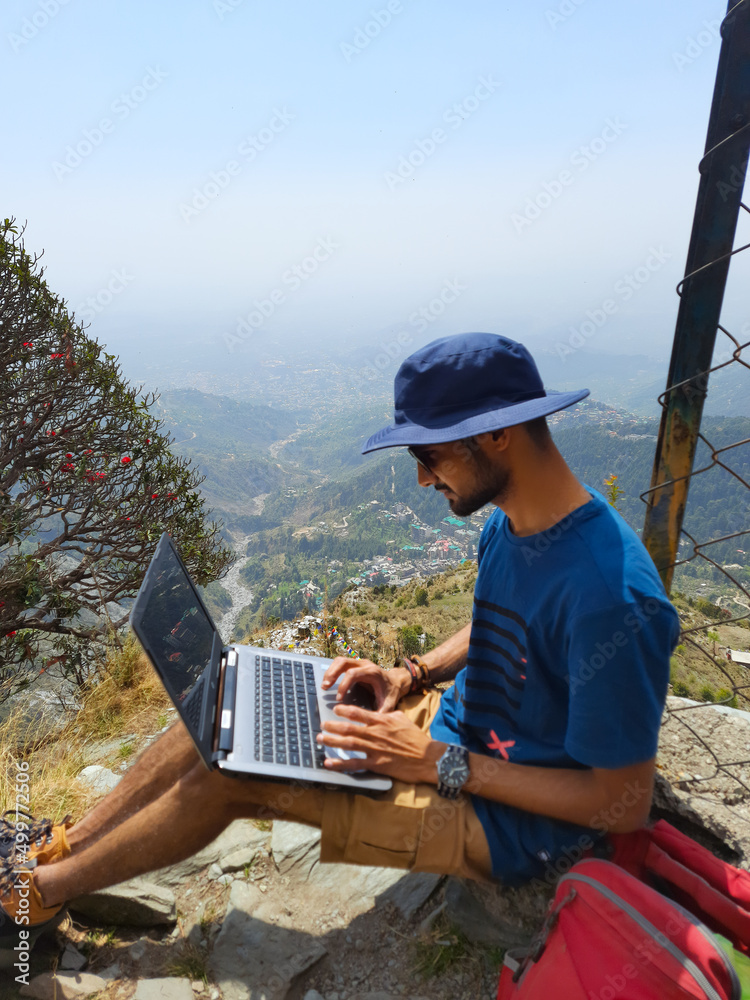 Young Man sitting alone outdoor with Laptop and mountains on background , Triund Top, Himachal Pradesh, India.
