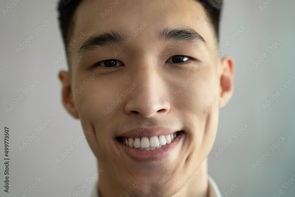 Asian man with dimples smiles widely raising eyebrow in room on blurred background. Portrait of young attractive guy looking in camera closeup Asian man with dimples smiles widely raising eyebrow in room on blurred background. Portrait of young attractive guy looking in camera closeup
