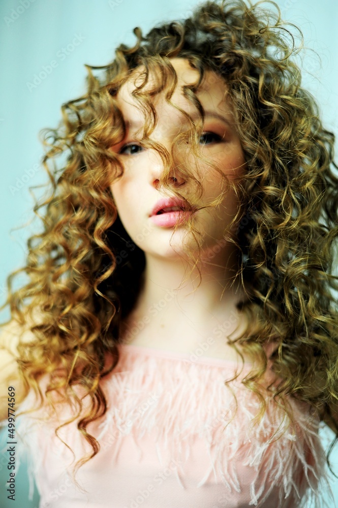 curly chic girl looks languid gaze mouth slightly open on her pink top with feathers of the eye a little with an oriental cut and hair light brown face and close-up hairstyle. High quality photo curly chic girl looks languid gaze mouth slightly open on her pink top with feathers of the eye a little with an oriental cut and hair light brown face and close-up hairstyle. High quality photo