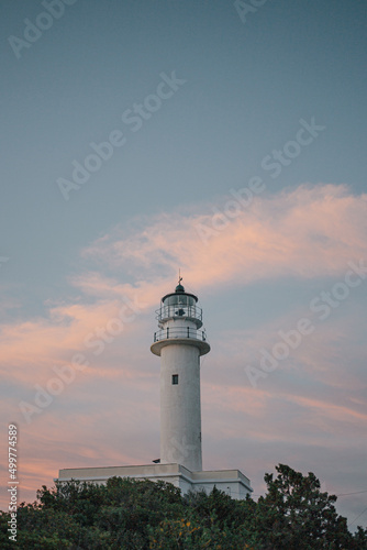 old lighthouse on a heel near the coastline with beautiful sunset sky.