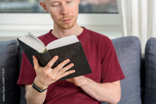 Bald hairless man reading book sitting on couch