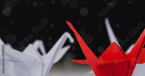 Image of spots falling over origami red and white birds on black background