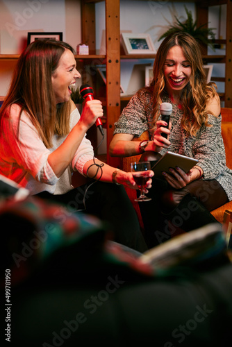 Two beautiful young women are singing karaoke at a home party.