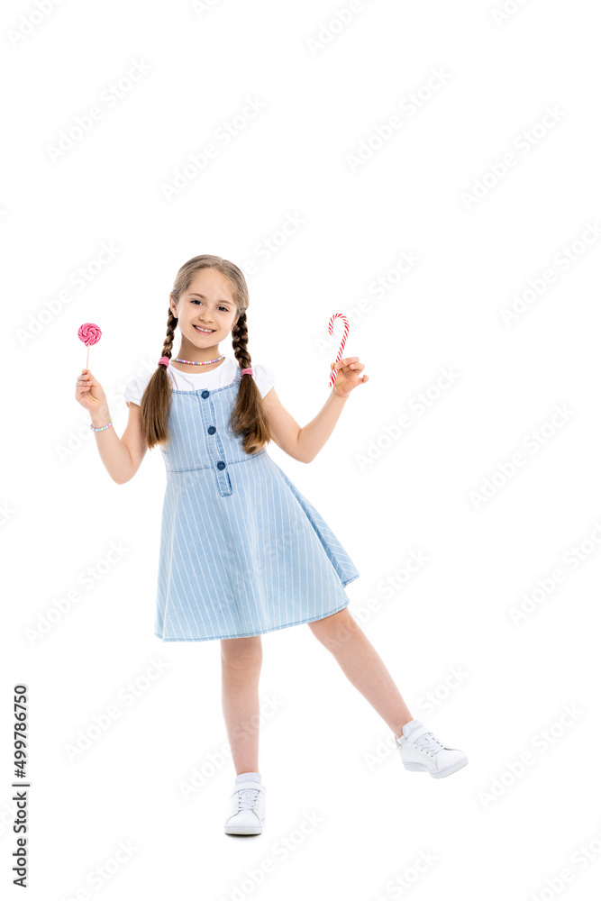 full length view of cheerful girl with candy cane and lollipop on white. full length view of cheerful girl with candy cane and lollipop on white.