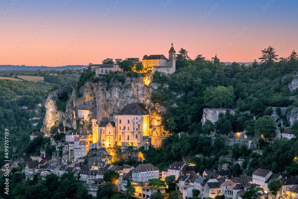 Majestic religious buildings of Rocamadour settlement lit with warm yellow illumination during twilight. Lot, Occitania, Southwestern France