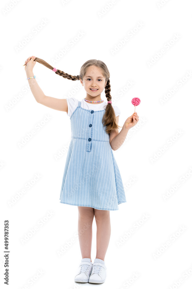 full length view of cheerful girl holding braid and lollipop on white. full length view of cheerful girl holding braid and lollipop on white.