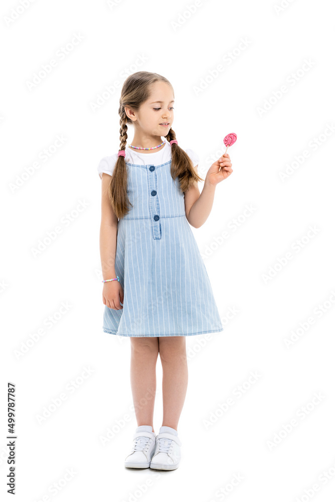 full length view of girl in blue strap dress looking at lollipop on white. full length view of girl in blue strap dress looking at lollipop on white.