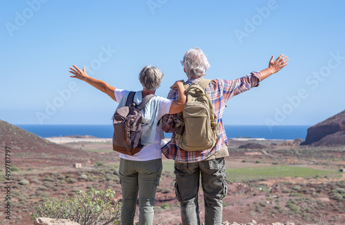 Active senior couple with outstretched arms in outdoors excursion hiking in mountain looking at horizon enjoying healthy lifestyle.  Scenic view of sea and mountain background