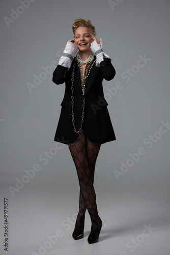 beautiful girl in fishnet tights and a black jacket with jewelry around her neck posing in the studio on a white background