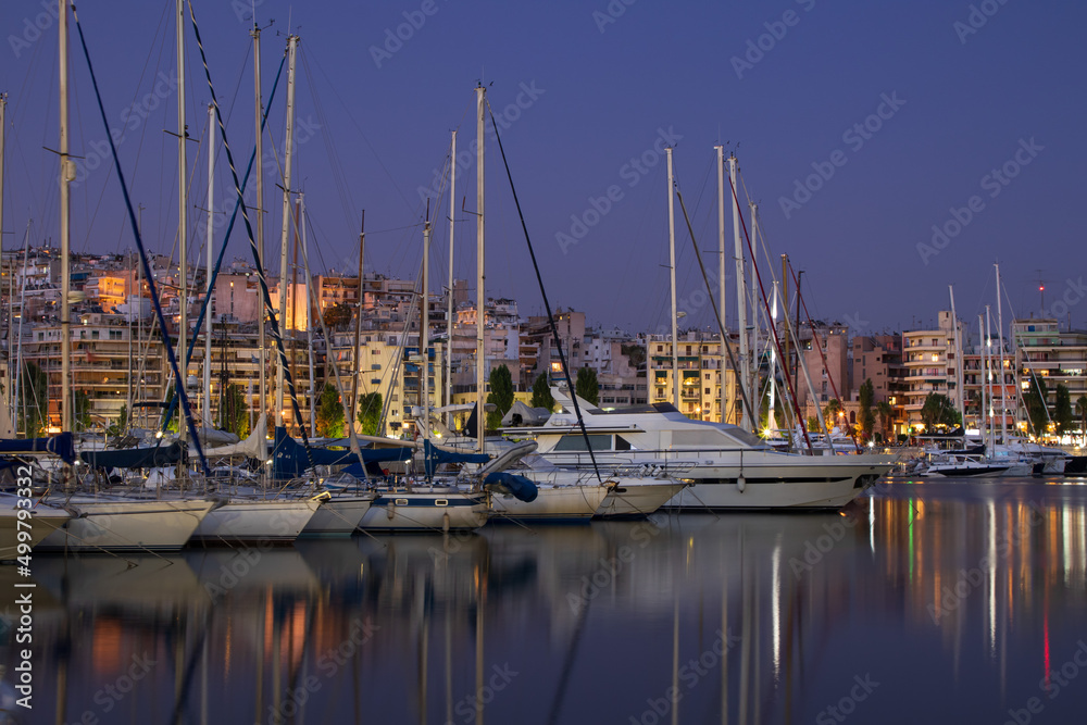 Luxury yachts and boats at the pier in a coastal town with night lights, from boats reflection on the water, Greece