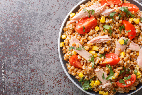 Delicious summer spelt salad with tuna, tomatoes and corn close-up in a plate on the table. Horizontal top view from above