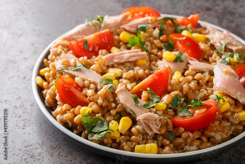 Fresh salad prepared with spelt, tuna, corn, tomatoes and herbs close-up in a plate on the table. horizontal
