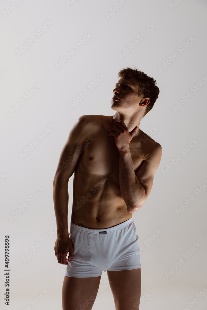 Silhouette of young shirtless muscled man wearing white boxer-briefs standing isolated on gray background. Natural beauty of male body. Emotions, love, care