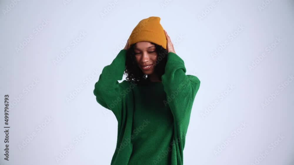 Handsome curly-haired woman wearing hat dancing in the grey studio Handsome curly-haired woman wearing hat dancing in the grey studio