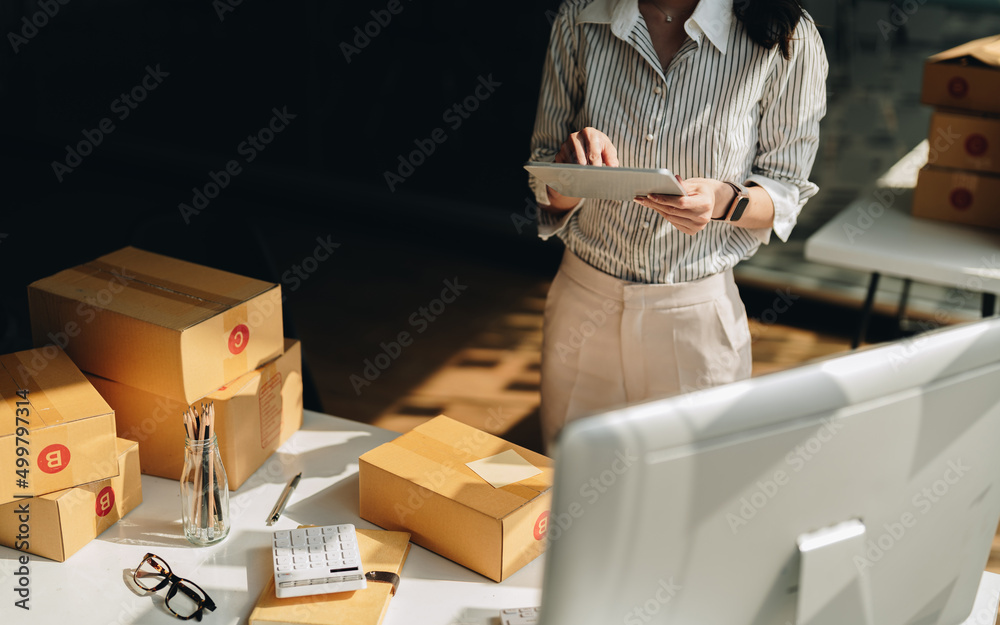 startup small business owner working with digital tablet at home. freelance woman seller check product order, packing goods for delivery. Online selling, e-commerce, shipping concept - obrazy, fototapety, plakaty 