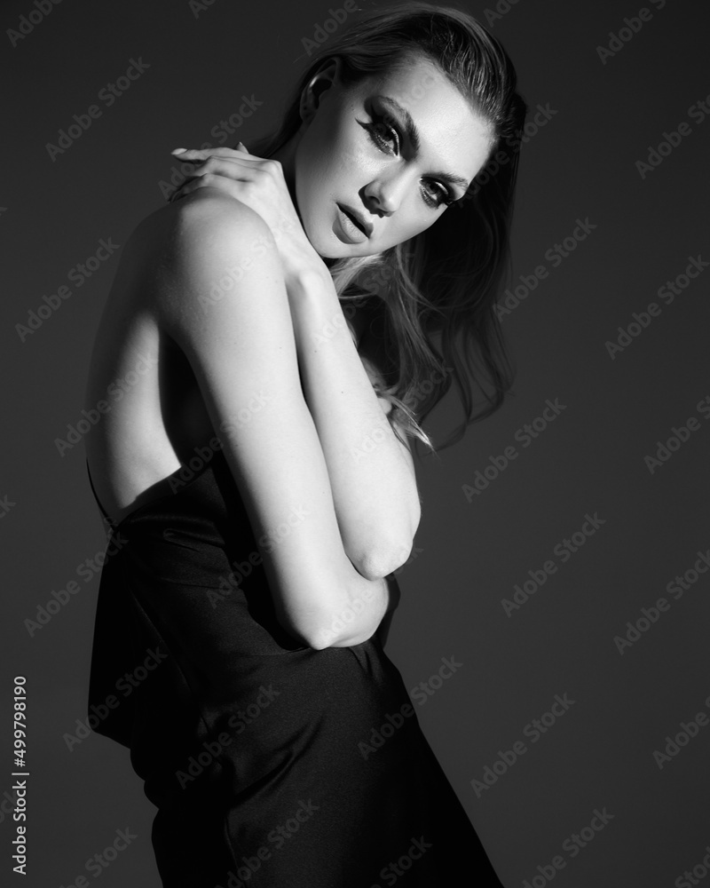 Young sexy fashionable blonde woman with long legs in designer 2022 trend evening short black silk dress. Vogue beauty glamour style. Studio shot. Creative light Young sexy fashionable blonde woman with long legs in designer 2022 trend evening short black silk dress. Vogue beauty glamour style. Studio shot. Creative light