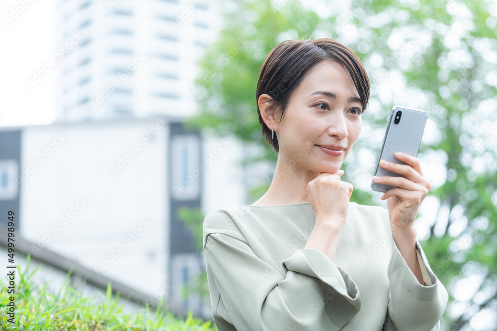 スマホを使うミドル女性（新緑・屋外）