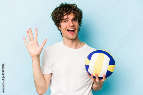 Young caucasian man playing volleyball isolated on blue background smiling cheerful showing number five with fingers.