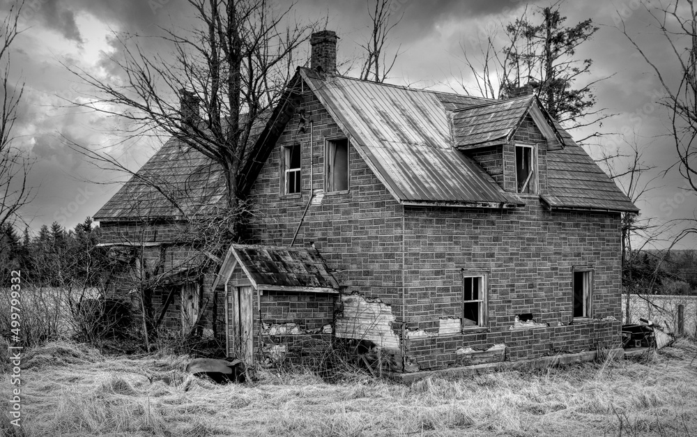 An old black and white abandoned spooky looking house in winter on a farm yard in rural Ontario, Canada