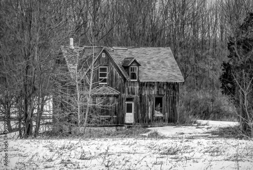 An old black and white abandoned spooky looking farmhouse in winter on a farm yard in rural Ontario, Canada