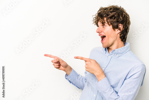 Young caucasian man isolated on white background points with thumb finger away, laughing and carefree.