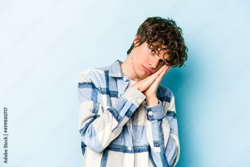 Young caucasian man isolated on blue background yawning showing a tired gesture covering mouth with hand. Young caucasian man isolated on blue background yawning showing a tired gesture covering mouth with hand.